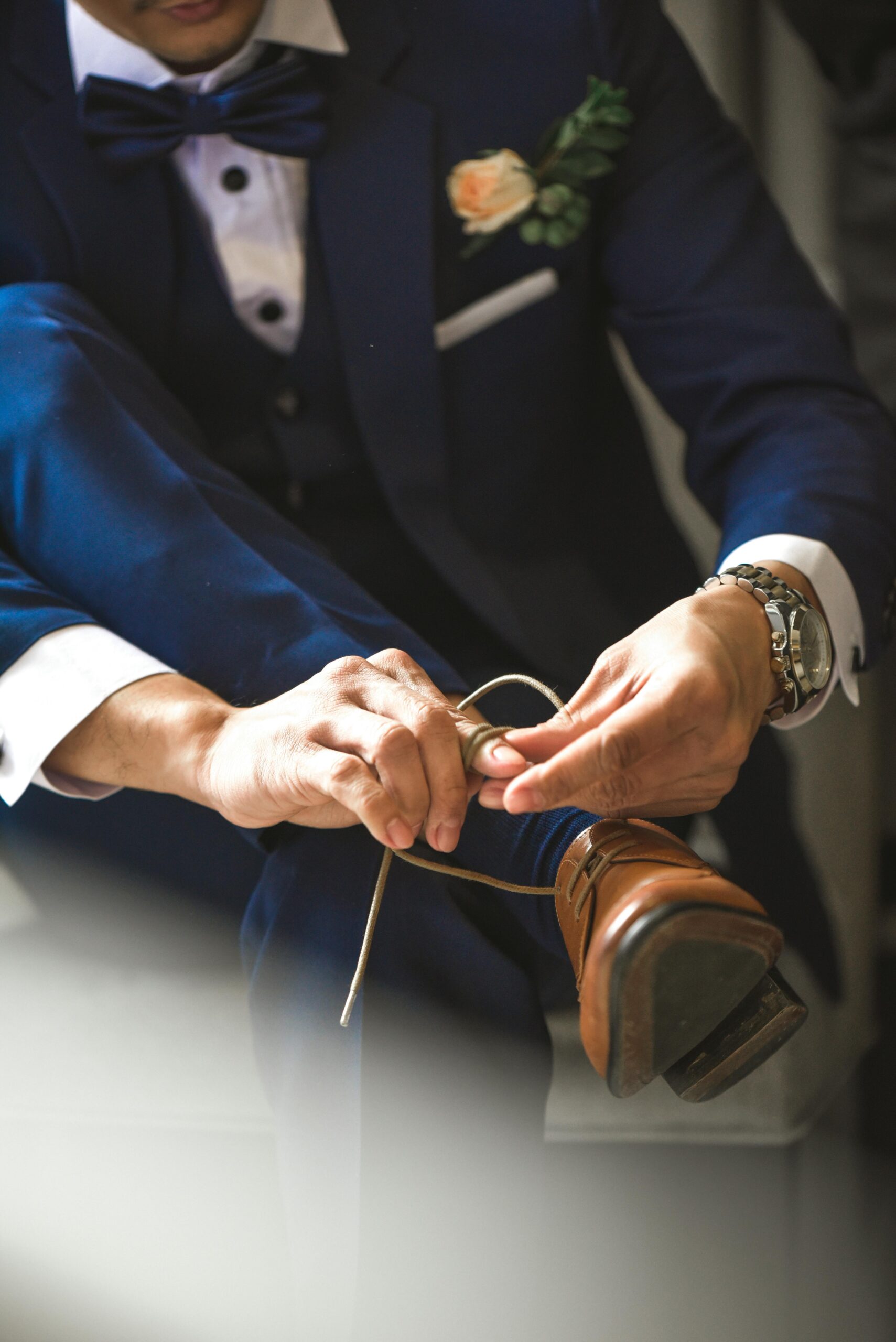 Close-up of a man in a suit tying his brown leather shoes, set indoors.